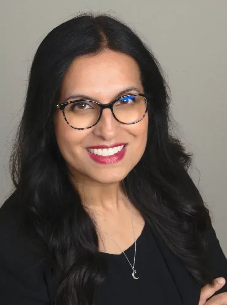 Woman with long dark hair, glasses, and a smiling expression.
