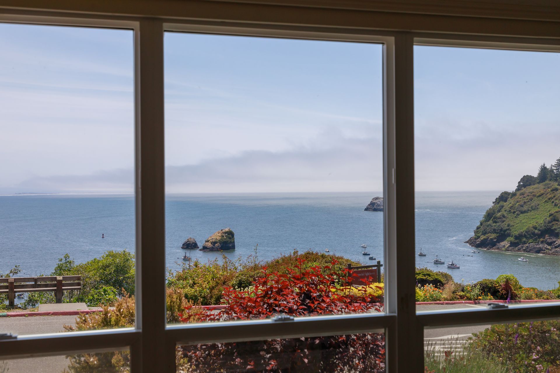 A view of the ocean through a window with a bench in the background