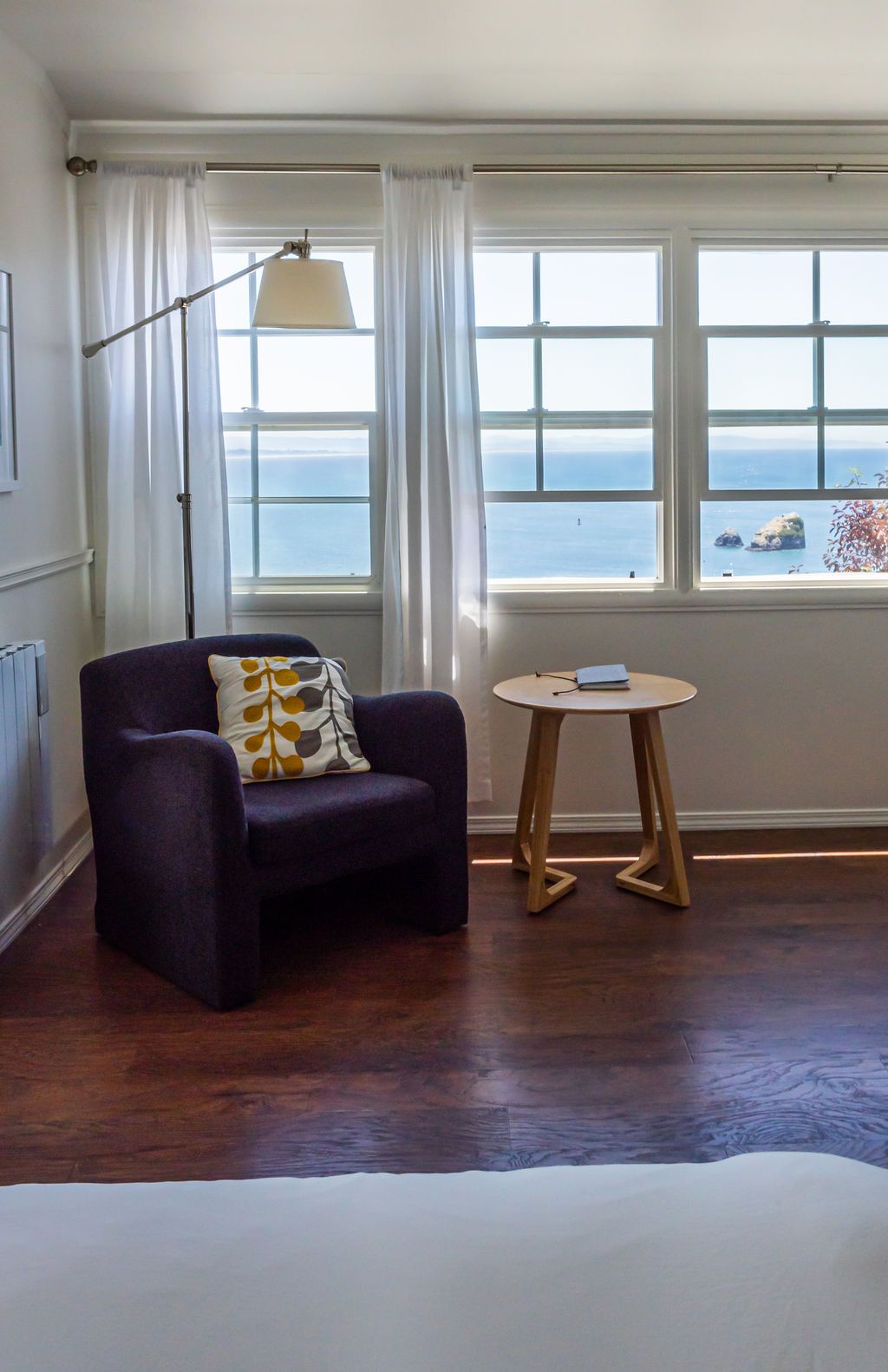 There is a chair and a table in the room with a view of the ocean.
