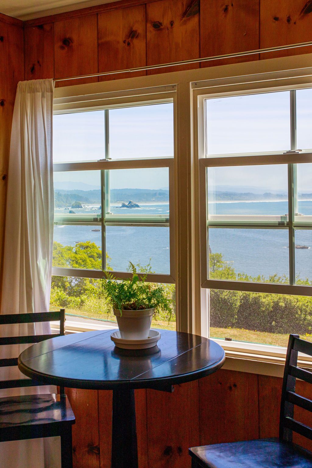 A table and chairs in front of a window with a view of the ocean.