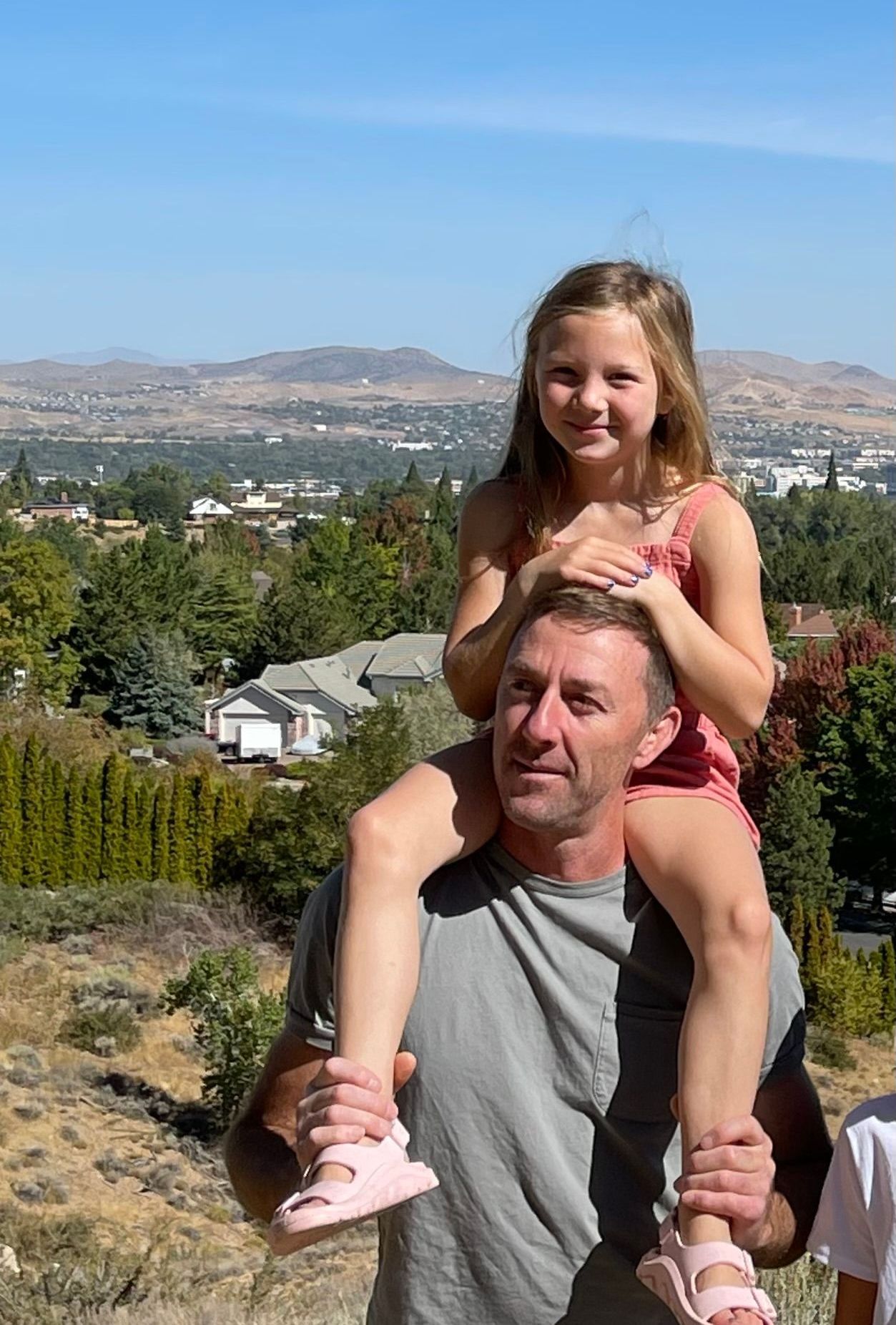 A man is carrying a little girl on his shoulders.