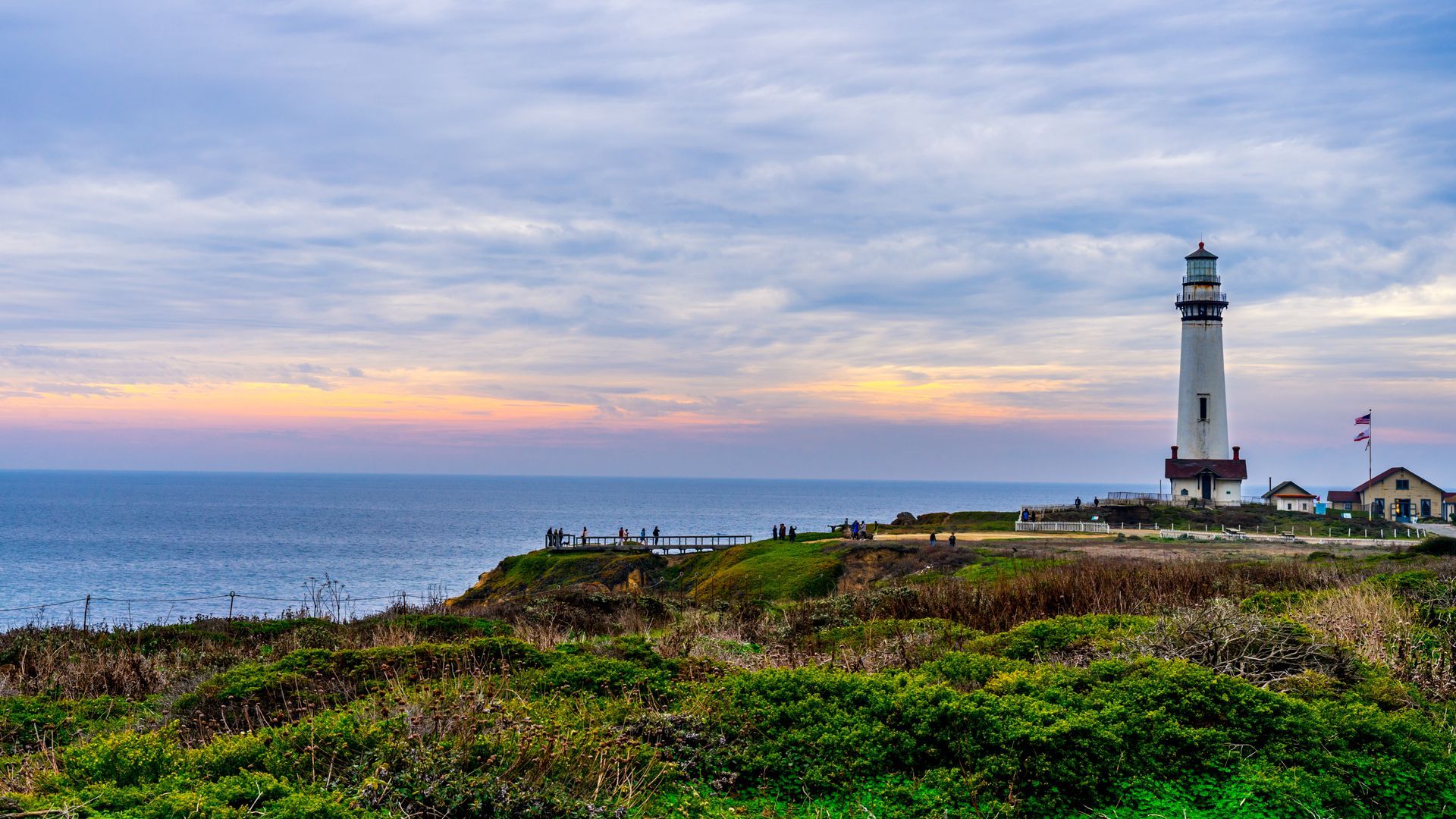 Lighthouse on a cliff overlooking the ocean at sunset with cloudy sky.