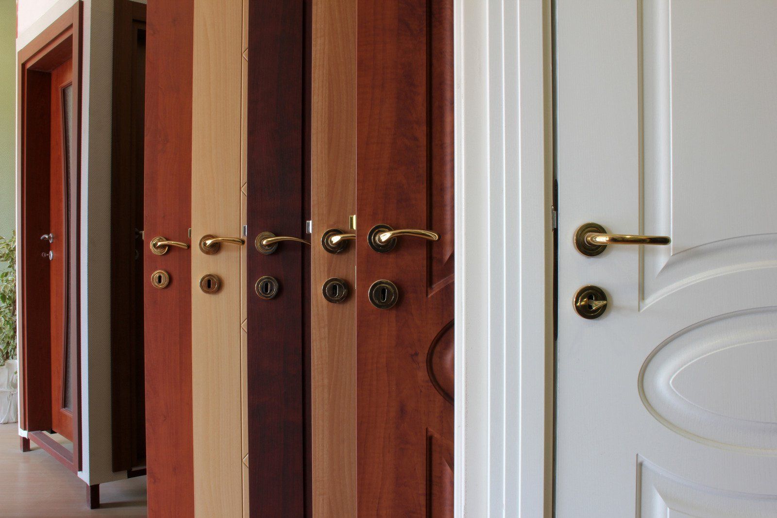 Row of open doors in a hallway, showing different wood and white finishes with brass handles