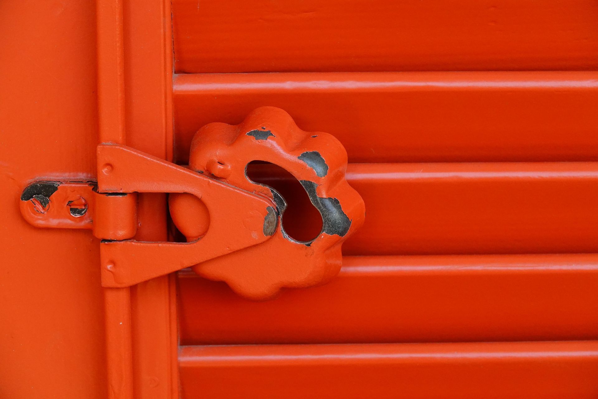 Orange metal door latch secured with a padlock on a corrugated orange shutter