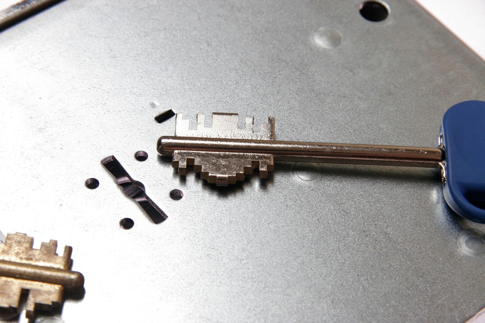 Broken key inside a lock with fragments scattered on a metal surface. Blue handled key also in the lock.