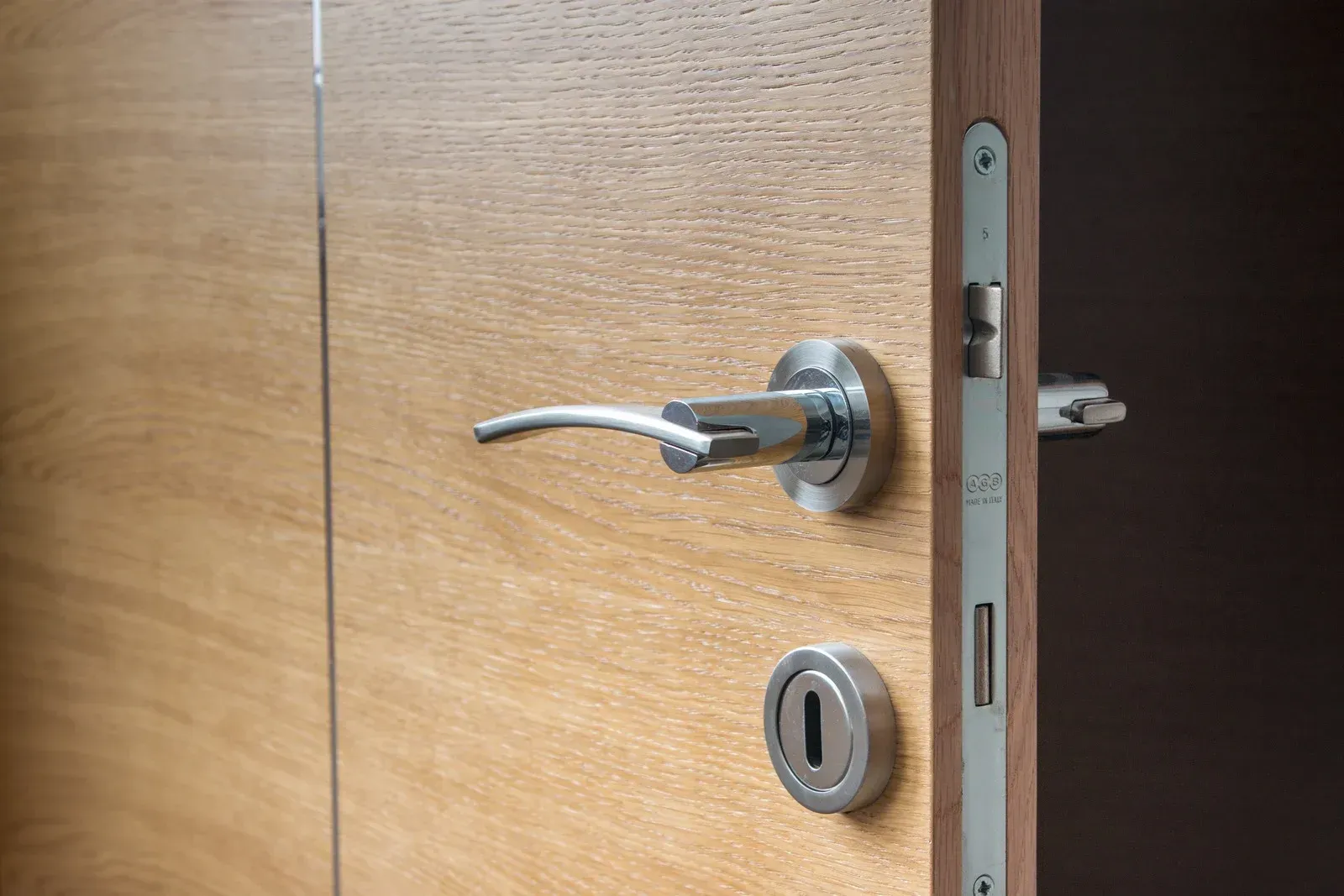 Wooden door with silver lever handle and lock, slightly open to a dark room