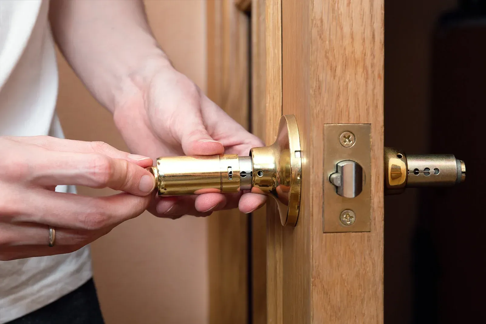 Person installing a gold door handle on a wooden door.