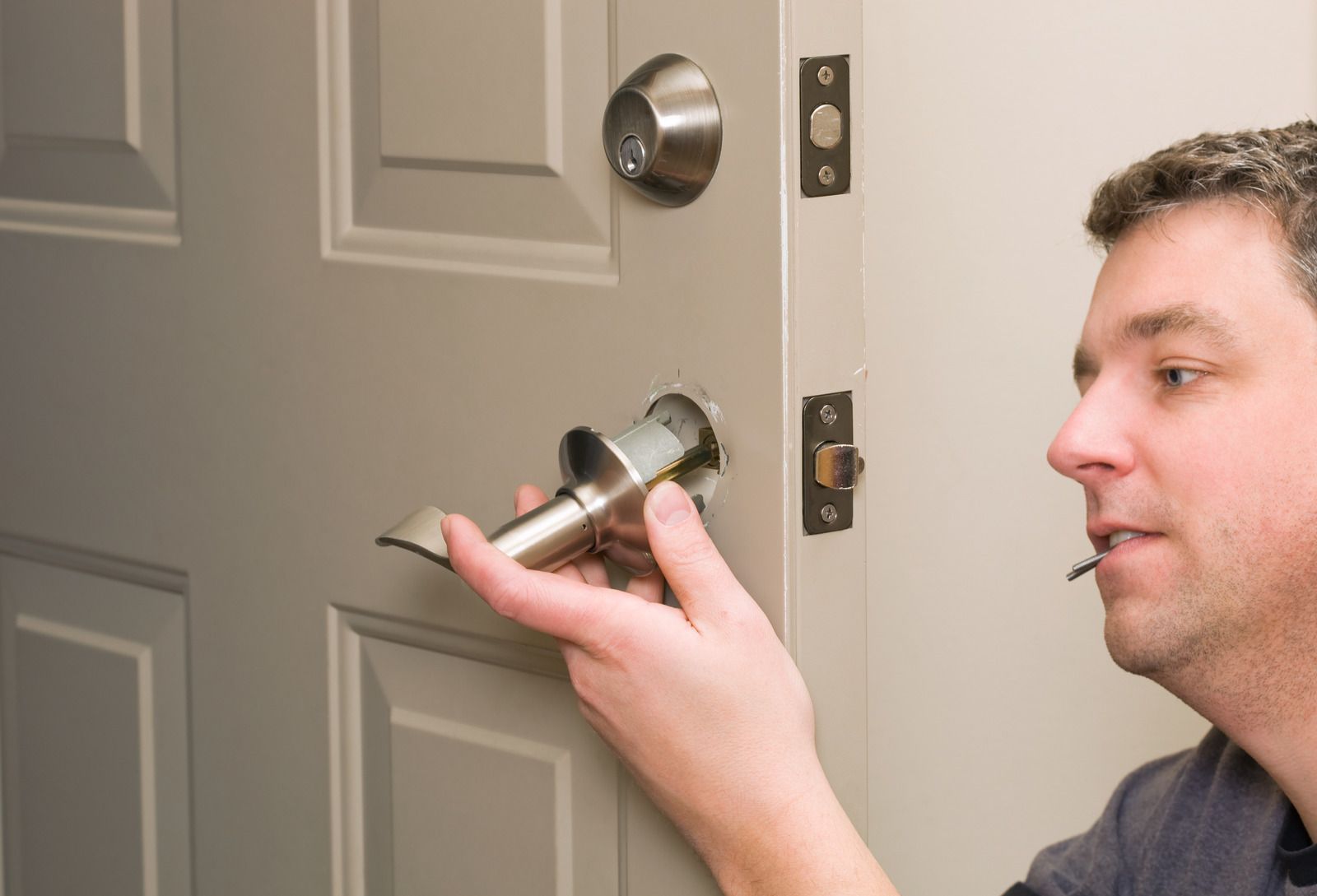 Person using a screwdriver to repair a doorknob on a wooden door.