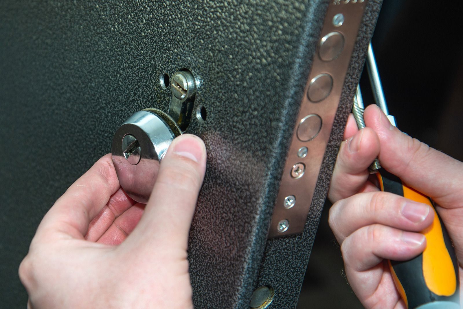 Hands installing a door lock cylinder with a screwdriver.