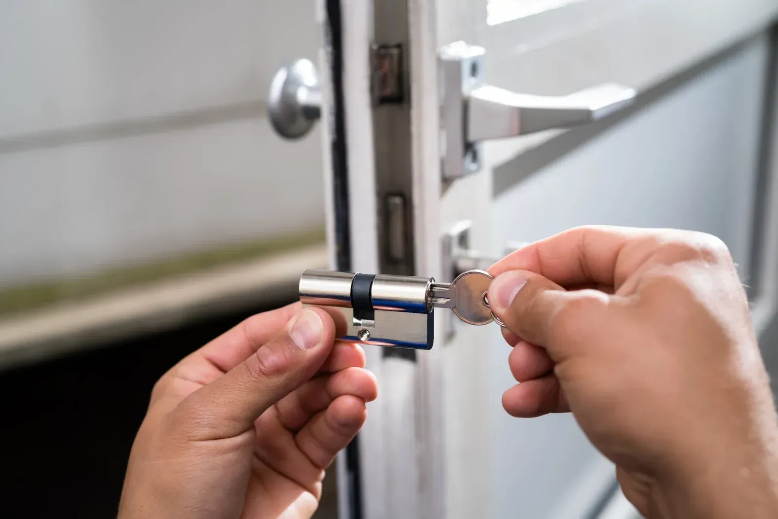Hands inserting a key into a silver door lock on a white door.
