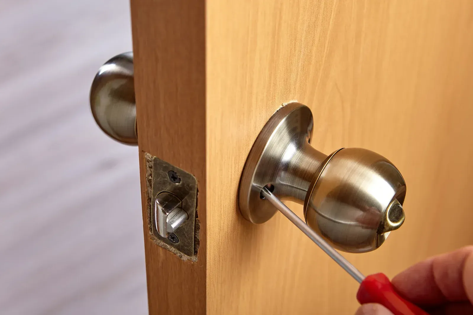 Person using a screwdriver to repair a doorknob on a wooden door.