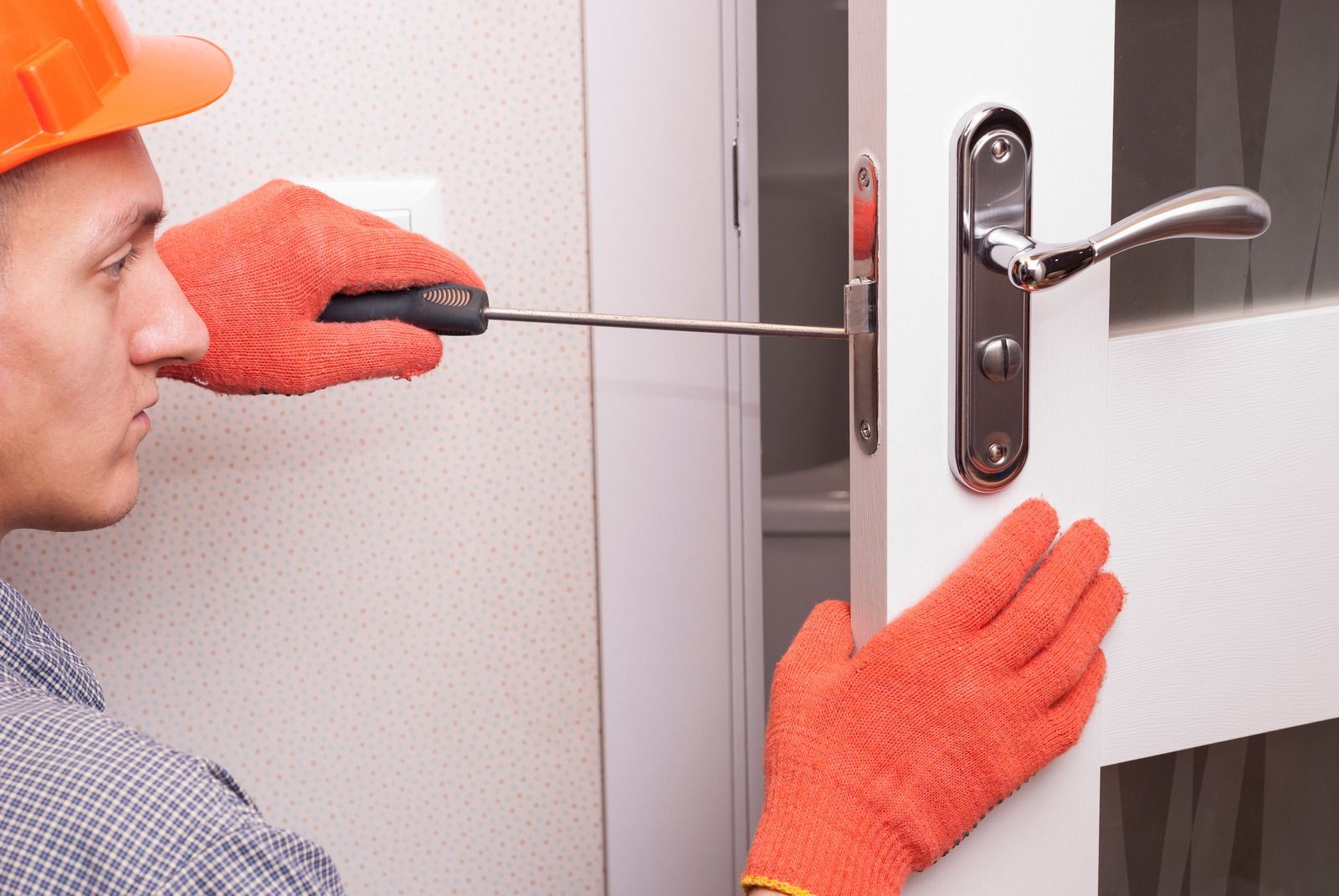 Person using a screwdriver to repair a doorknob on a wooden door.