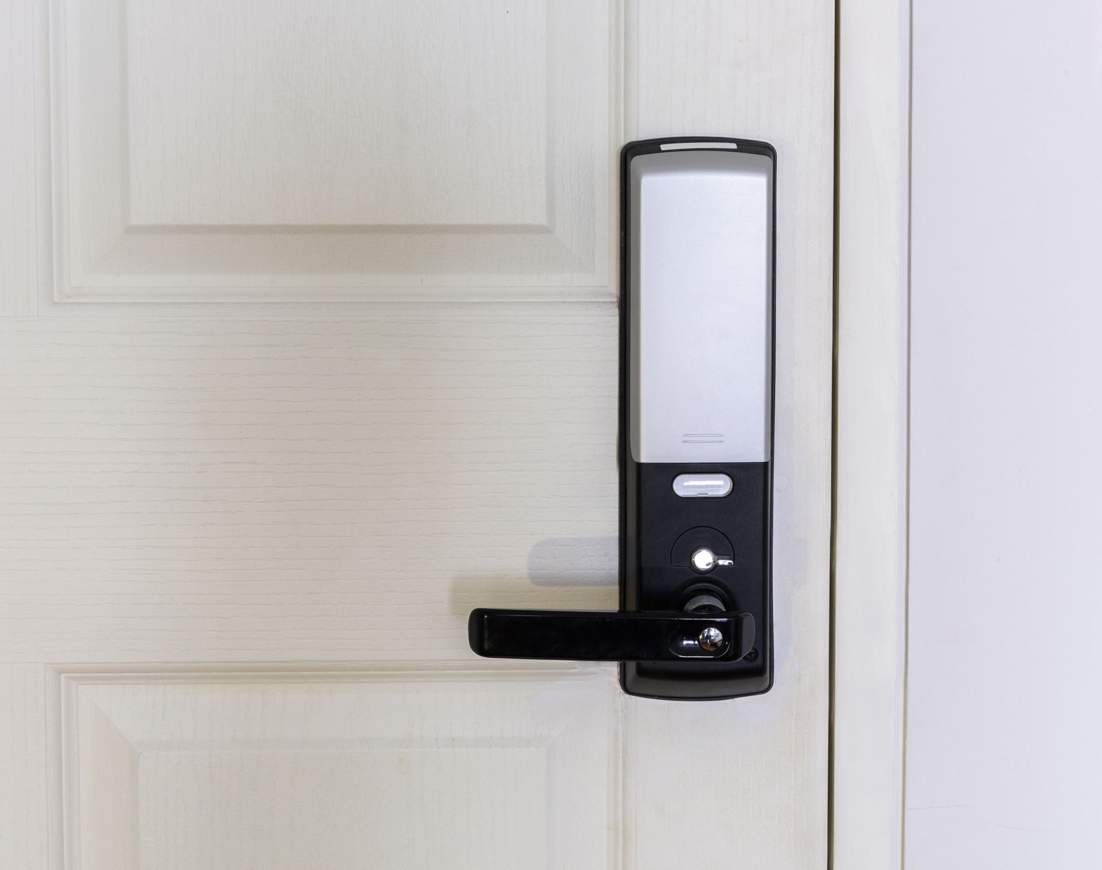 Black smart door lock on a white door. The door has a handle and is closed.