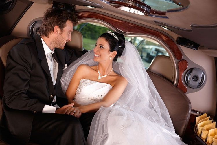 A bride and groom are sitting in the back of a limousine holding hands.