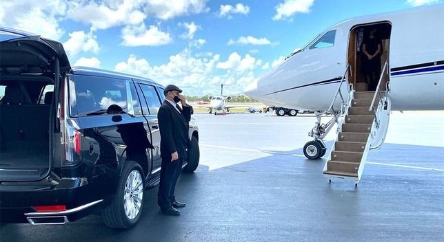 A man is standing next to a car in front of a private jet.