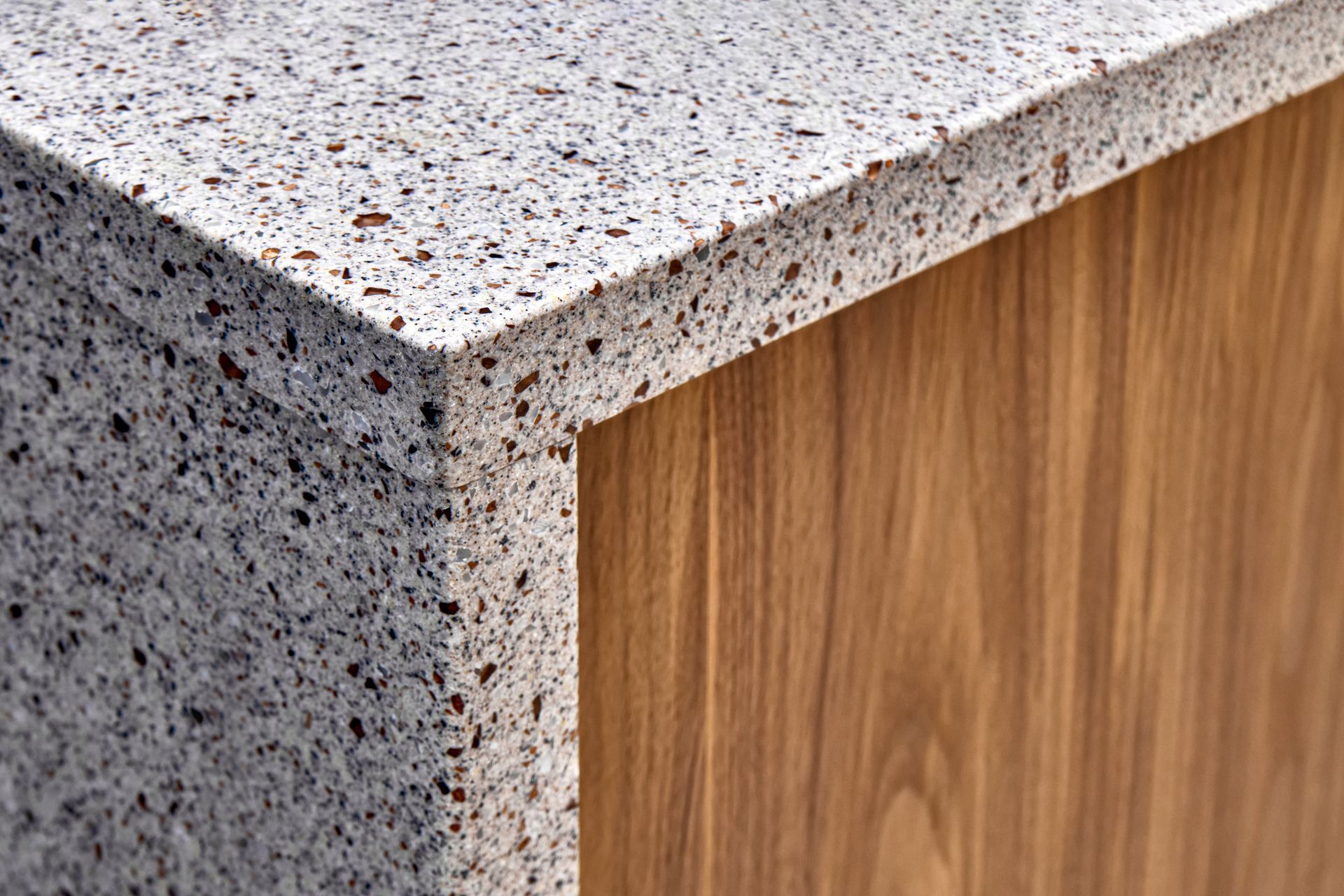 Close-up of polished stone benchtops on wooden cabinet, showcasing modern kitchen countertop design.