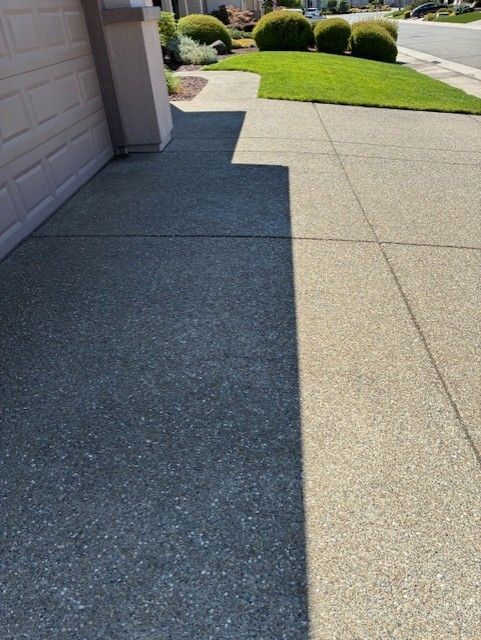 Cleanup King LLC - Concrete driveway with a shadowed area next to a beige building. Green lawn and bushes in the background.