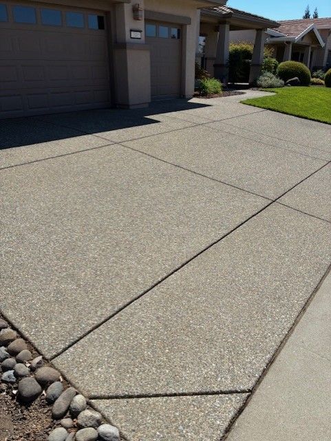 Cleanup King LLC - Concrete driveway with textured surface, bordered by rocks and grass, next to a house.