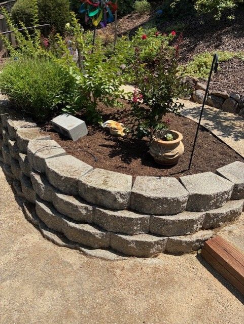 Cleanup King LLC - A stone retaining wall encloses a garden bed with plants and a terracotta pot on a sunny day.