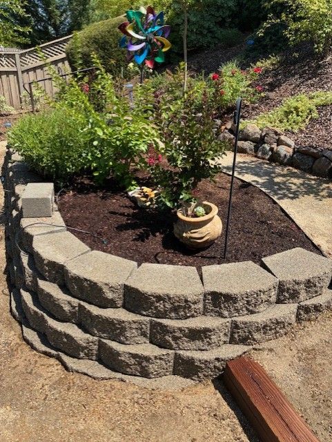 Cleanup King LLC - Stone-walled garden bed with brown mulch, green plants, and a decorative windmill.