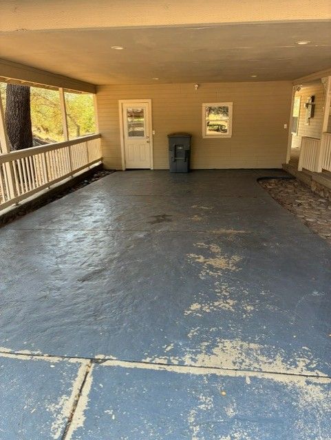 Cleanup King LLC - Covered carport with peeling blue floor, beige walls, door, window, and trash bin.