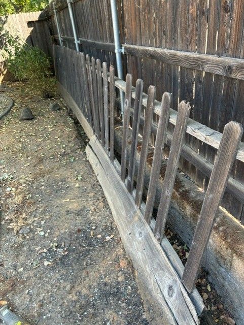 Cleanup King LLC - Wooden picket fence leaning against a weathered wooden fence, dirt ground, outdoor setting.