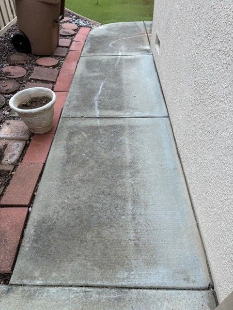 Cleanup King LLC - Concrete walkway next to a beige wall, dirtied with green and grey stains, edged by red bricks.