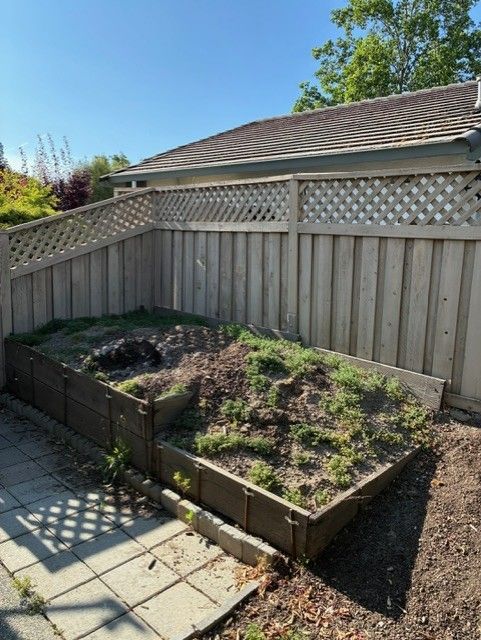 Cleanup King LLC - Raised garden bed with brown soil, weeds, and wood fence. Sunny day.