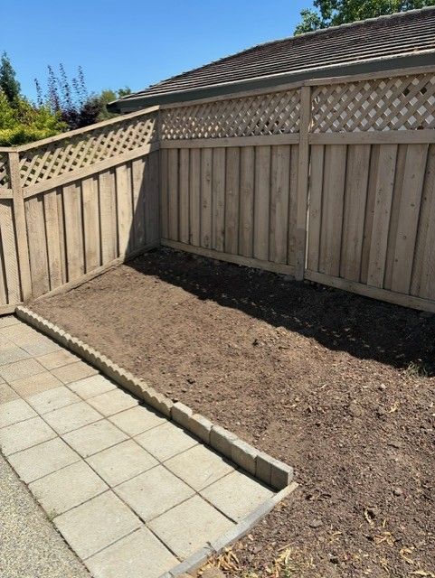 Cleanup King LLC - A small, empty garden bed with a concrete patio in a backyard, surrounded by a wooden fence.