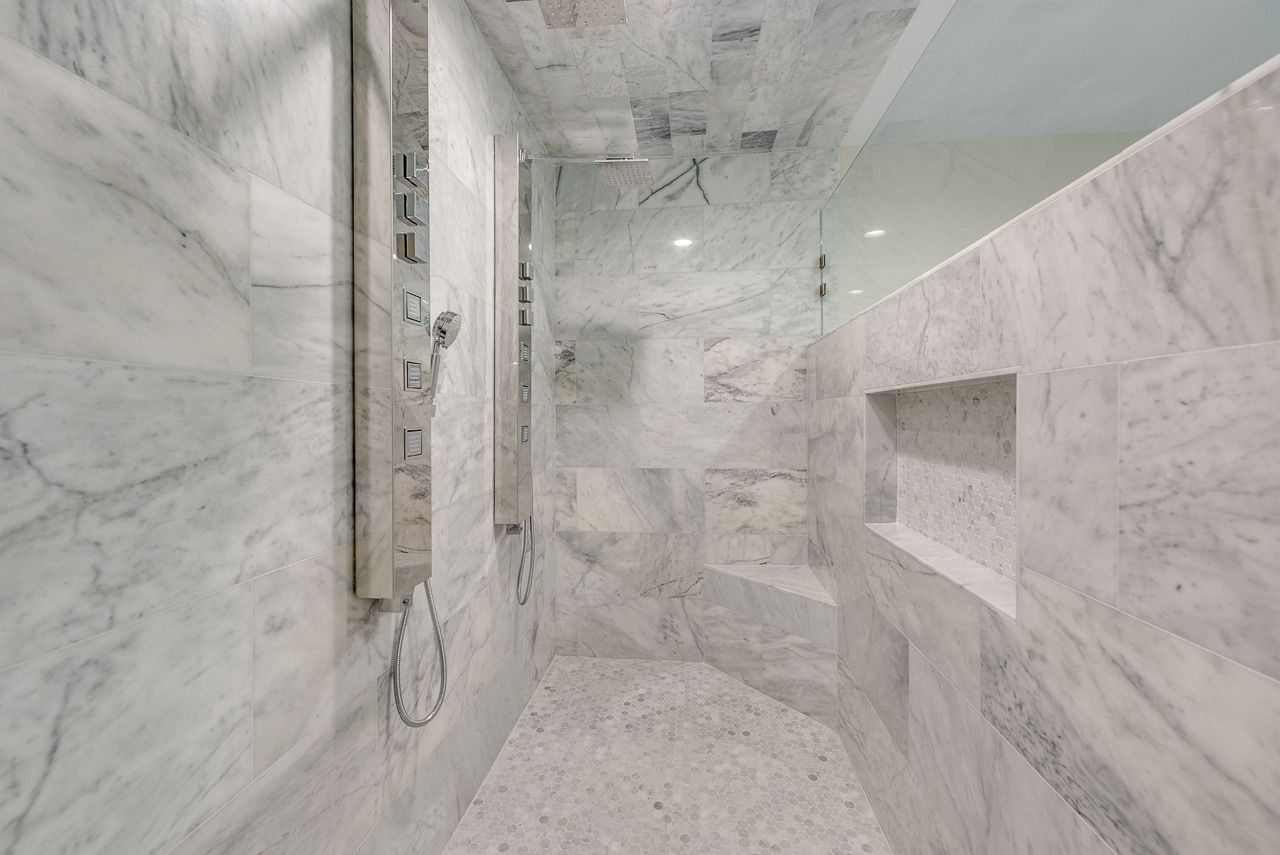 Beautiful modern shower renovation in Flower Mound, TX, by Night 'N' Day Construction, featuring Carrara marble, double spa showerheads, and body sprayers