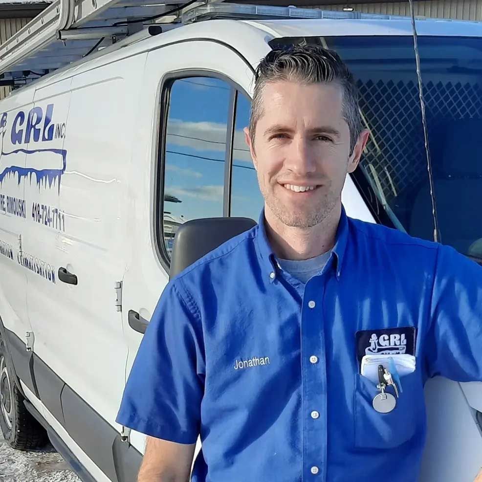 Un homme en chemise de travail bleue sourit à côté d'une camionnette blanche arborant le logo d'une entreprise.