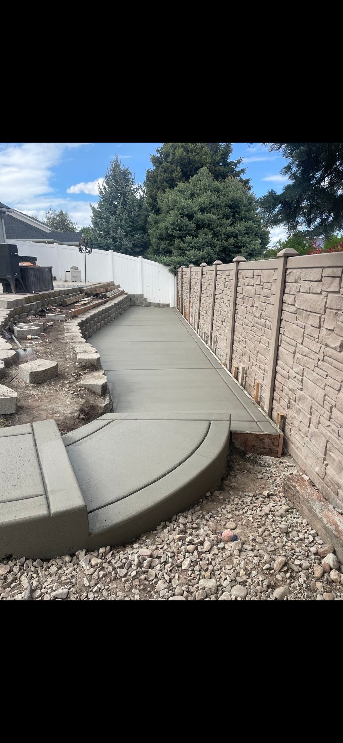 Curved concrete walkway beside a stone retaining wall and gravel yard under a blue sky Curved concrete walkway beside a stone retaining wall and gravel yard under a blue sky