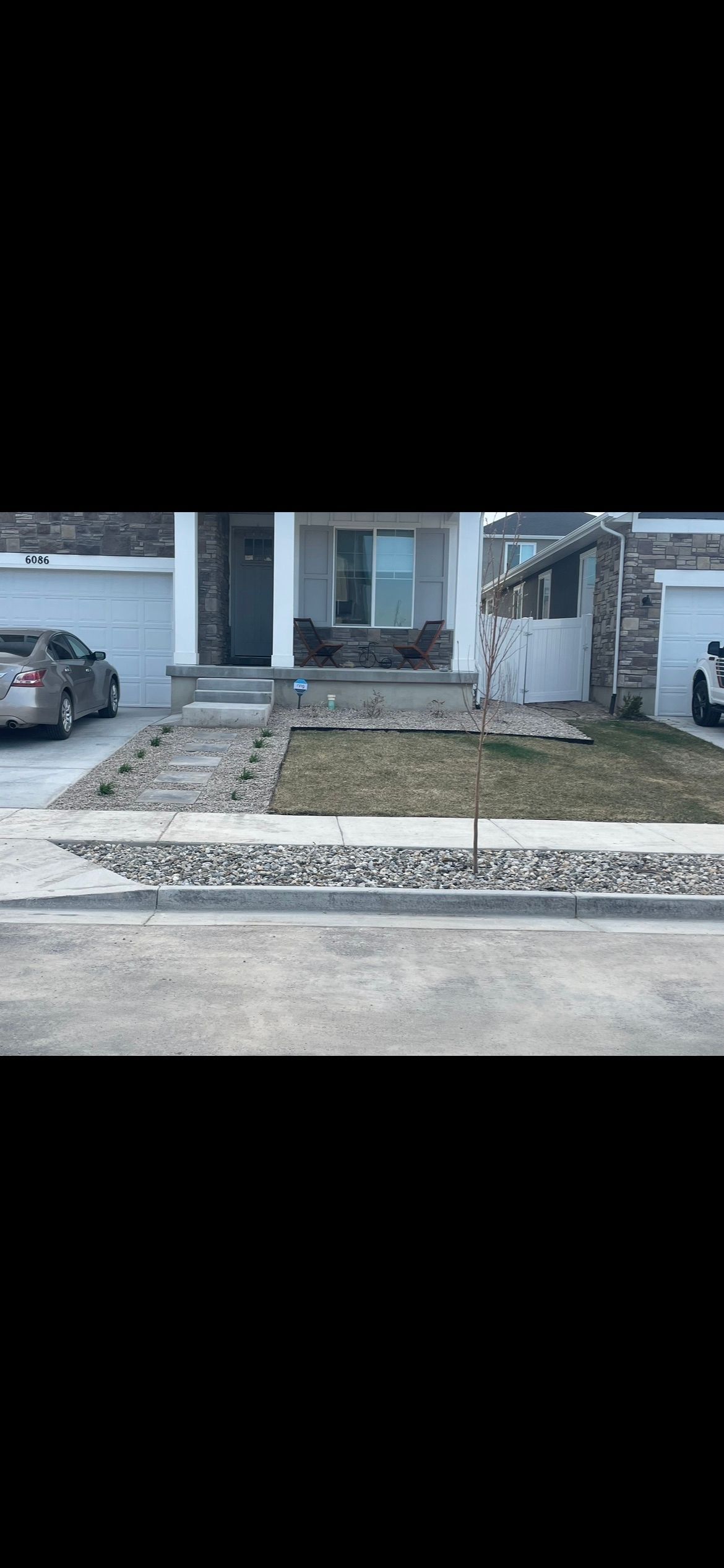Front yard with a concrete walkway, patchy grass, a parked car, and a house entrance under construction Front yard with a concrete walkway, patchy grass, a parked car, and a house entrance under construction