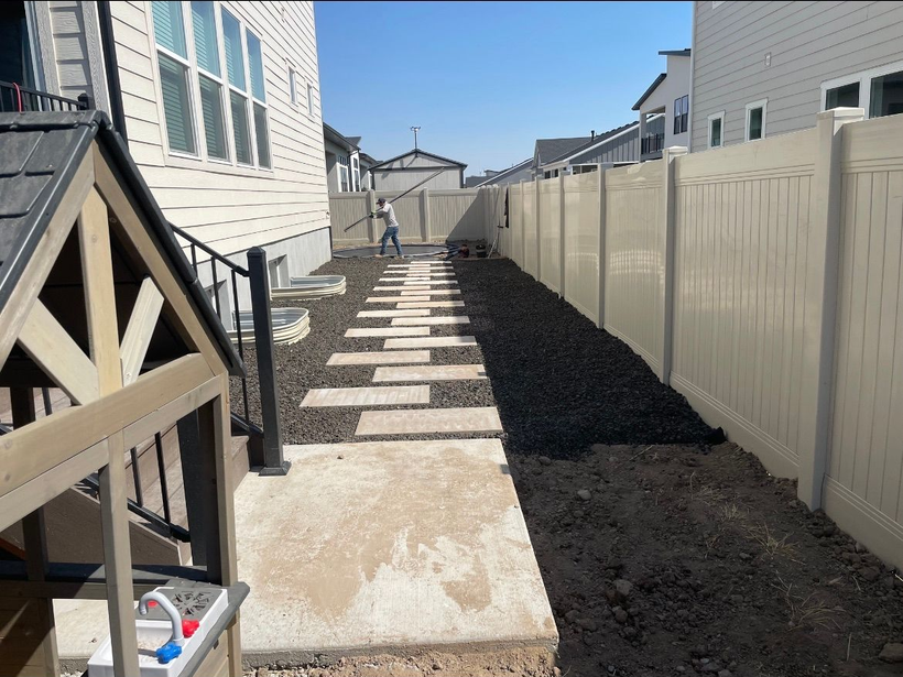 Narrow backyard walkway with concrete stepping stones, white fence, and dark mulch between houses Narrow backyard walkway with concrete stepping stones, white fence, and dark mulch between houses