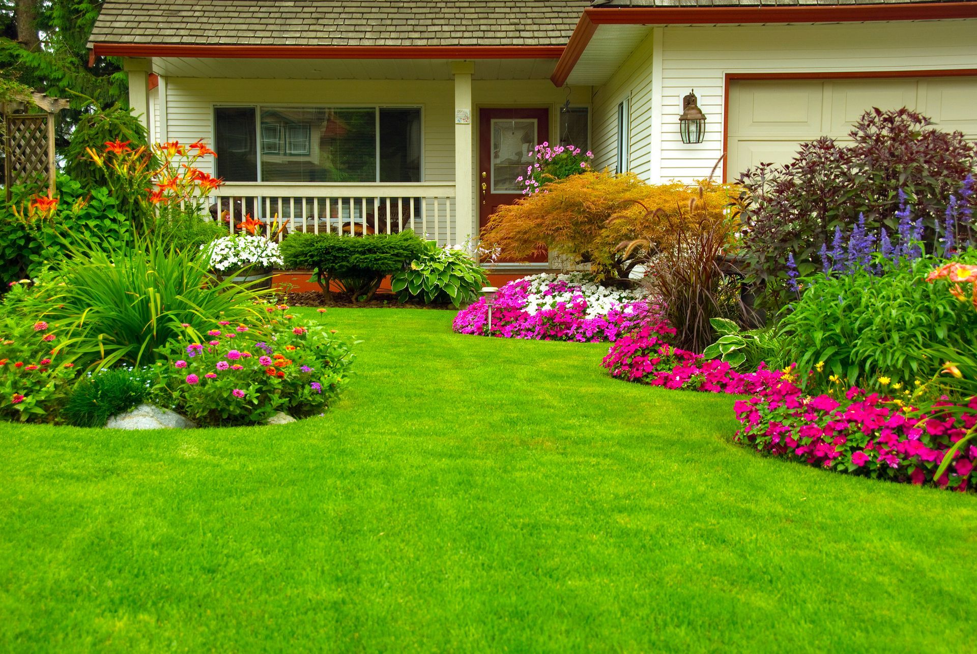 A stone water feature sits on artificial turf next to a path of white stone stepping stones leading to a flower bed.