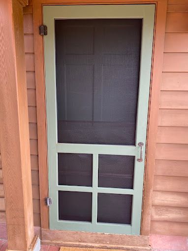 A green screen door is on the side of a house.