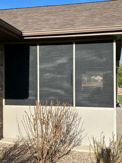 A house with a screened in porch and a bush in front of it.