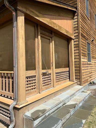 A screened in porch on the side of a wooden house.