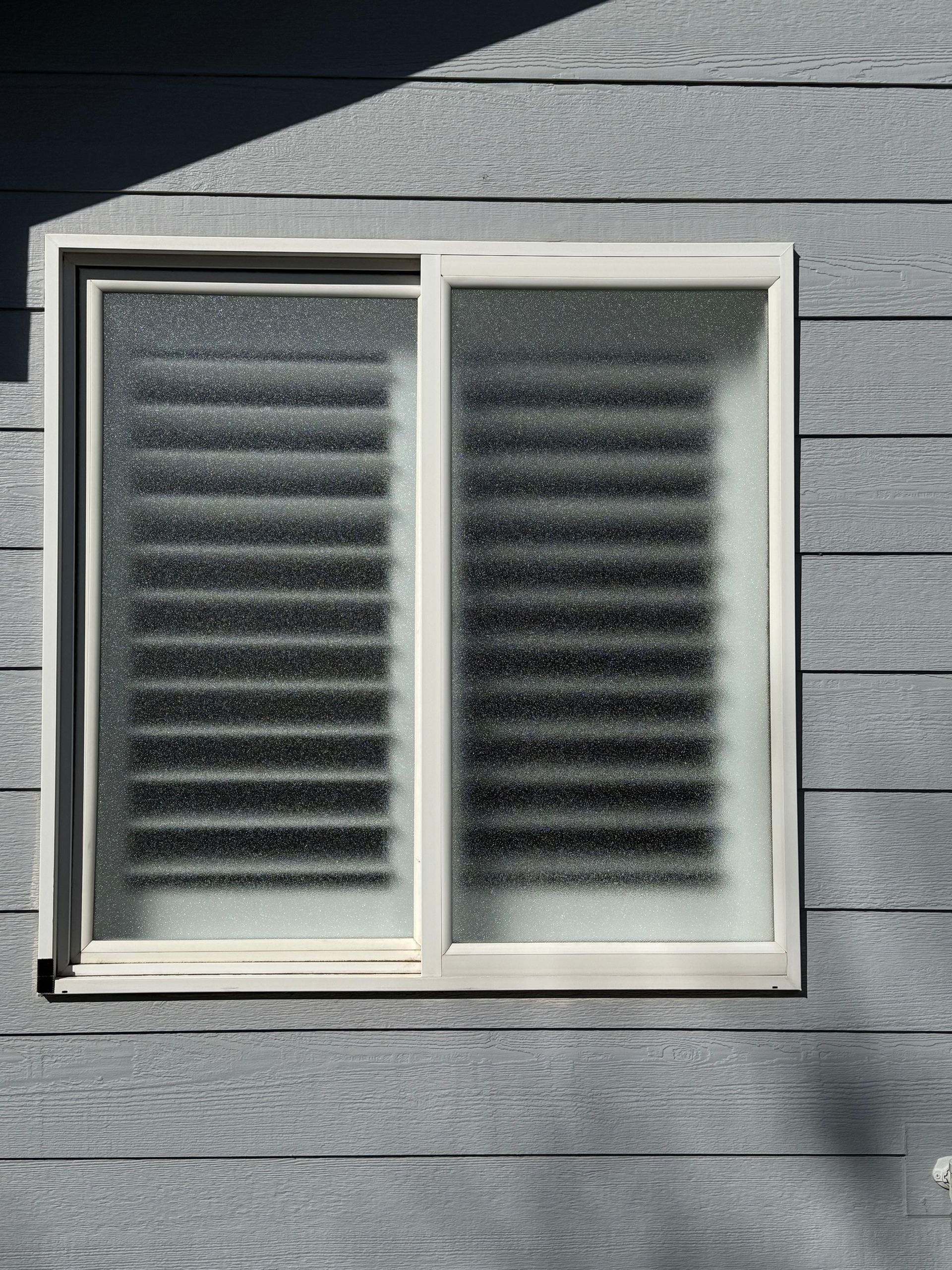 A window with shutters on it is on a gray wall.