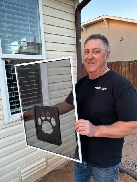 A man in a black shirt is holding a screen door with a paw print on it
