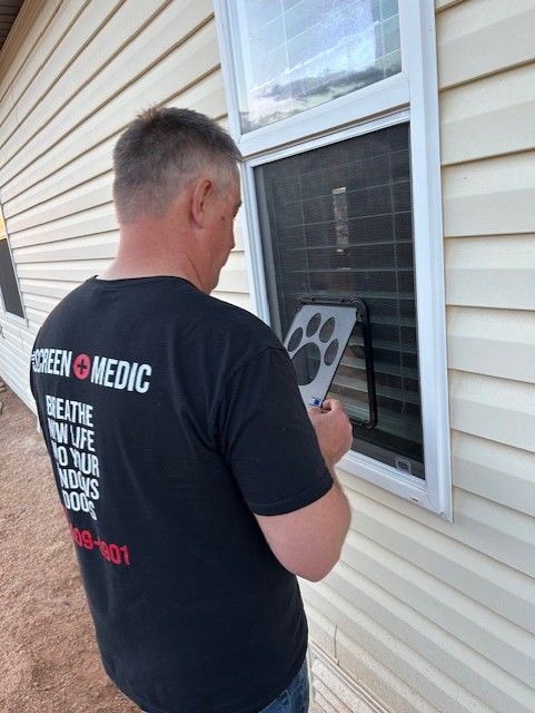 A man wearing a screen medic shirt is looking out a window
