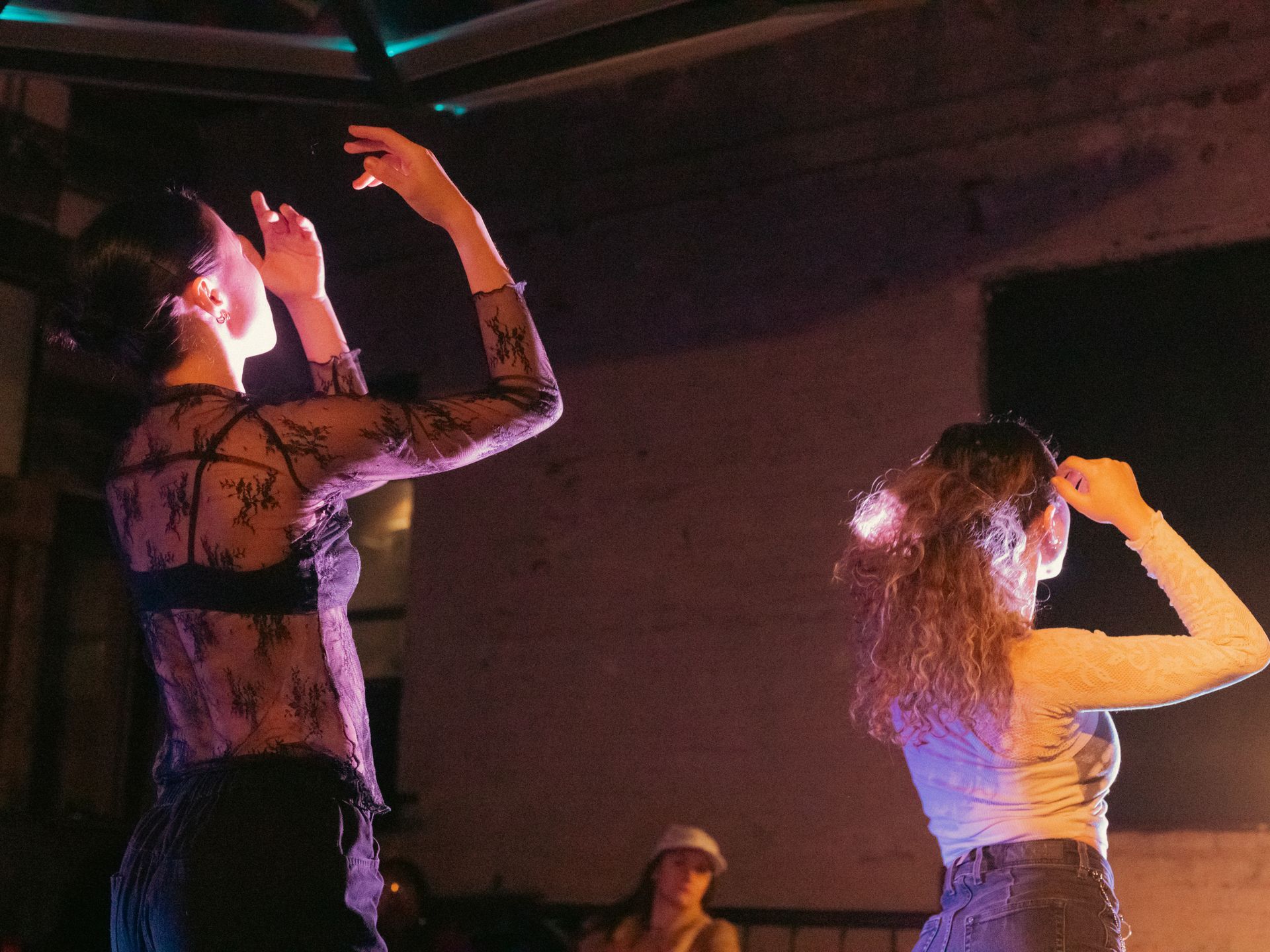 Two dancers performing on stage, arms raised. Low lighting, purple and blue hues.