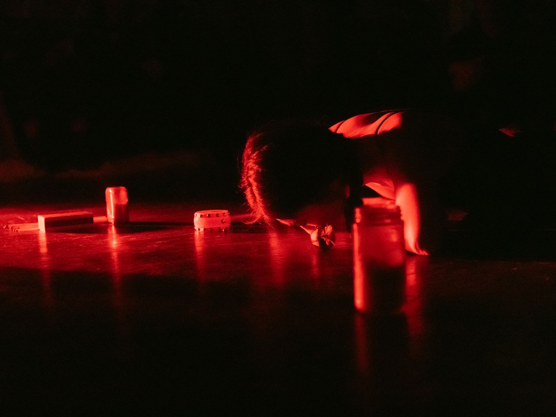 Person crawling on floor, illuminated by red light, approaching a row of blocks.