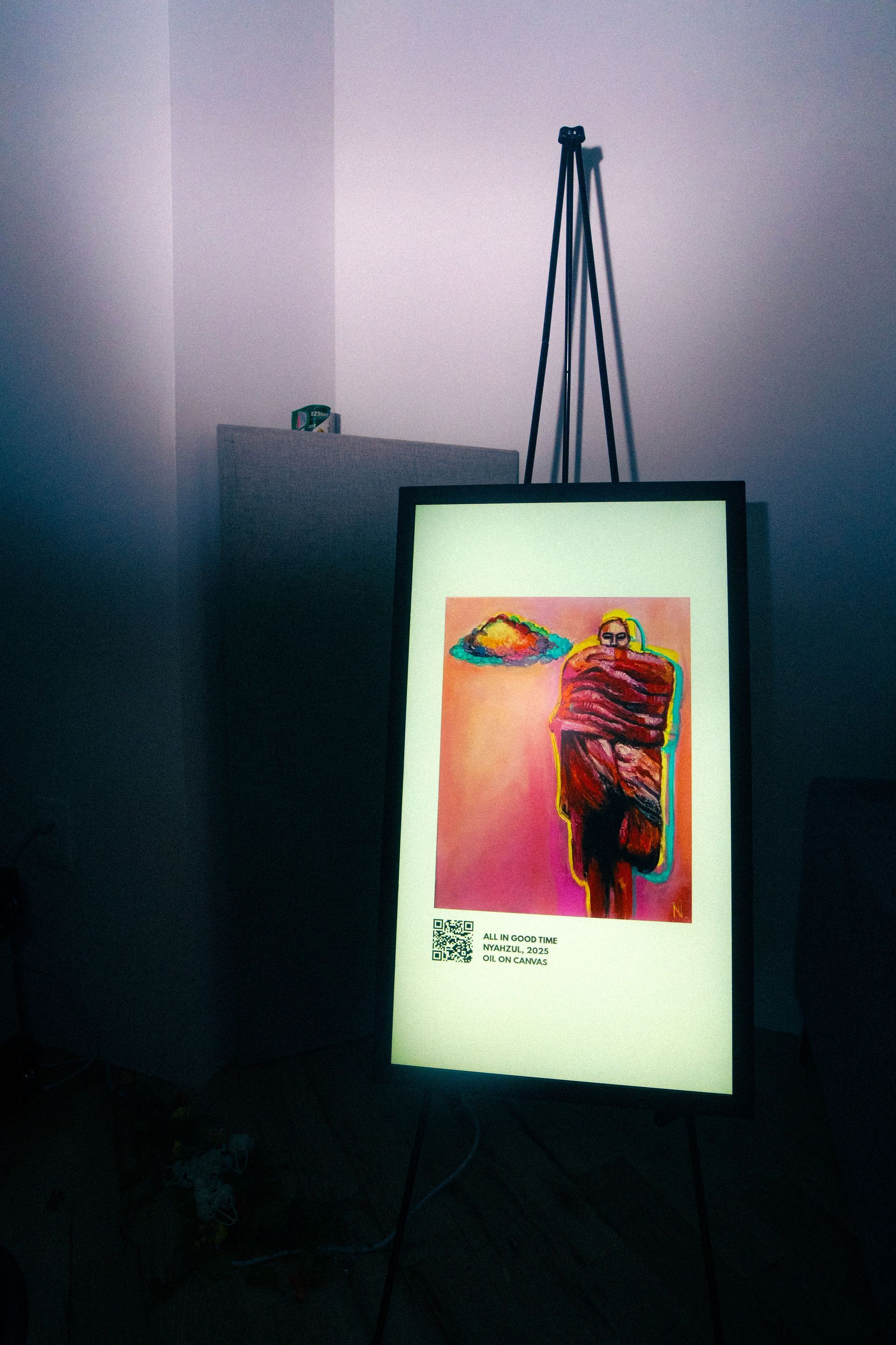 Artwork displayed on a light-up frame on an easel. Pink, orange, and purple hues. A figure with a QR code.