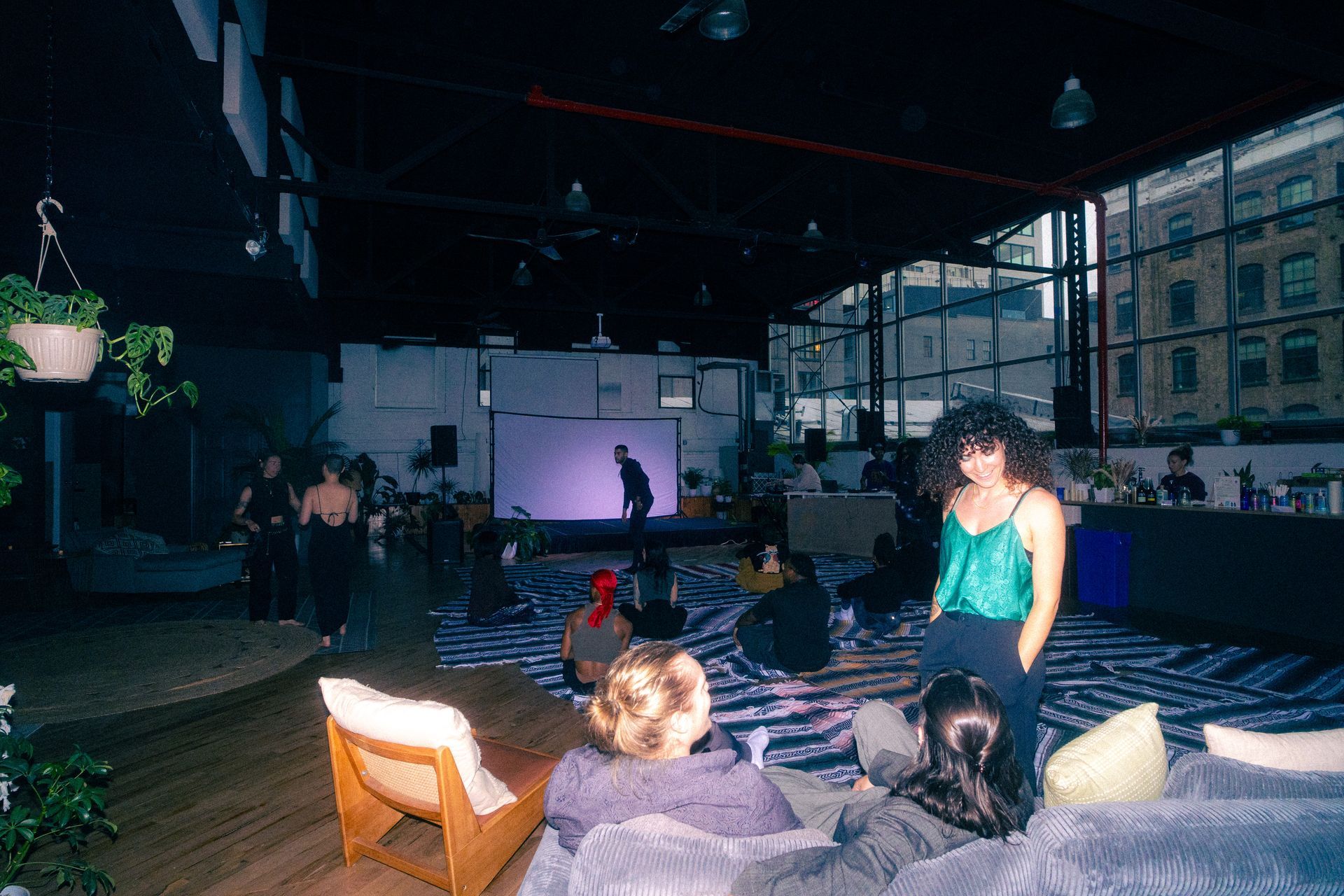 People in a large room with a projector screen. A woman in teal stands in front.