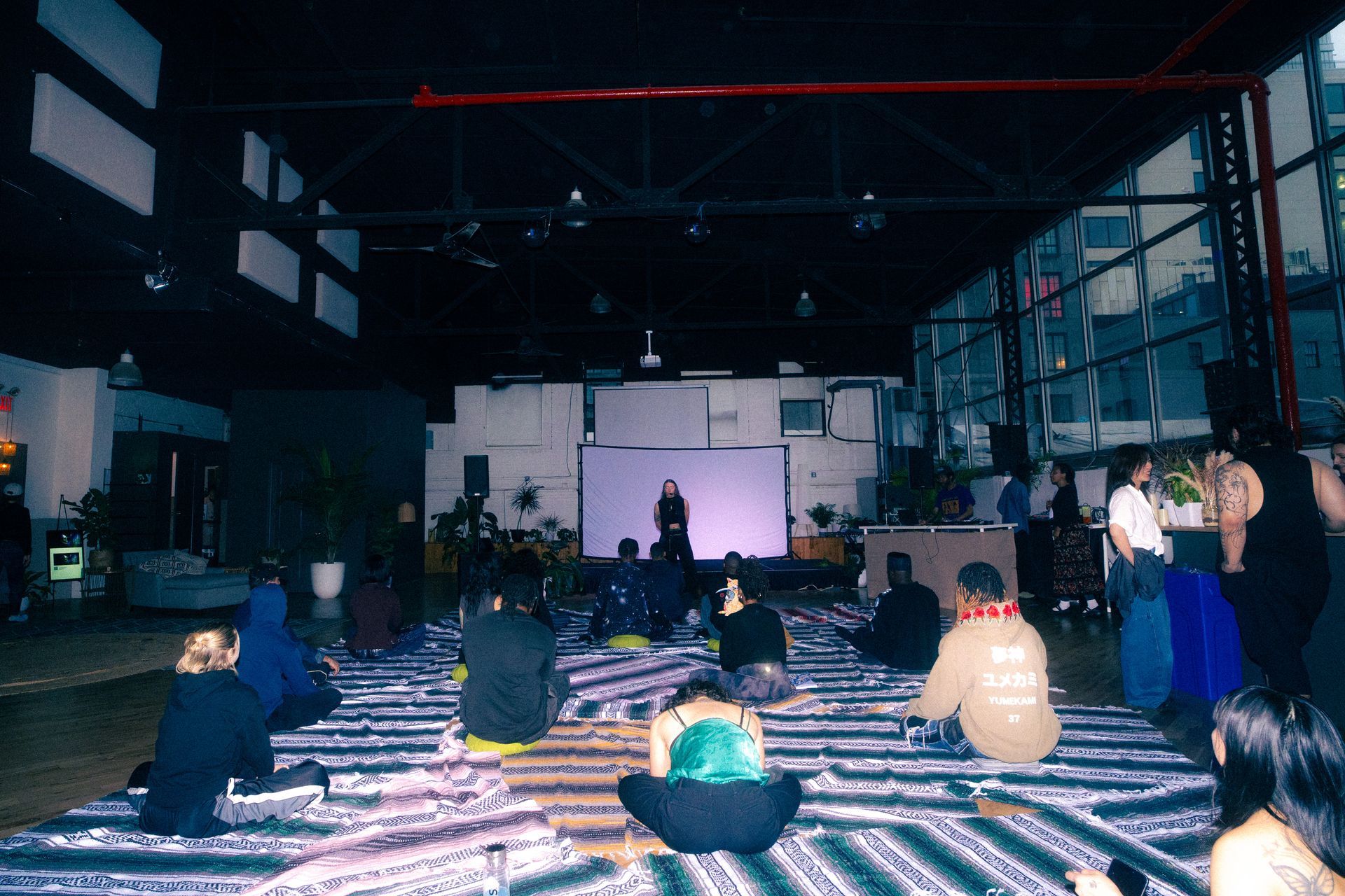 People seated on rugs, facing a presenter in a large open room.