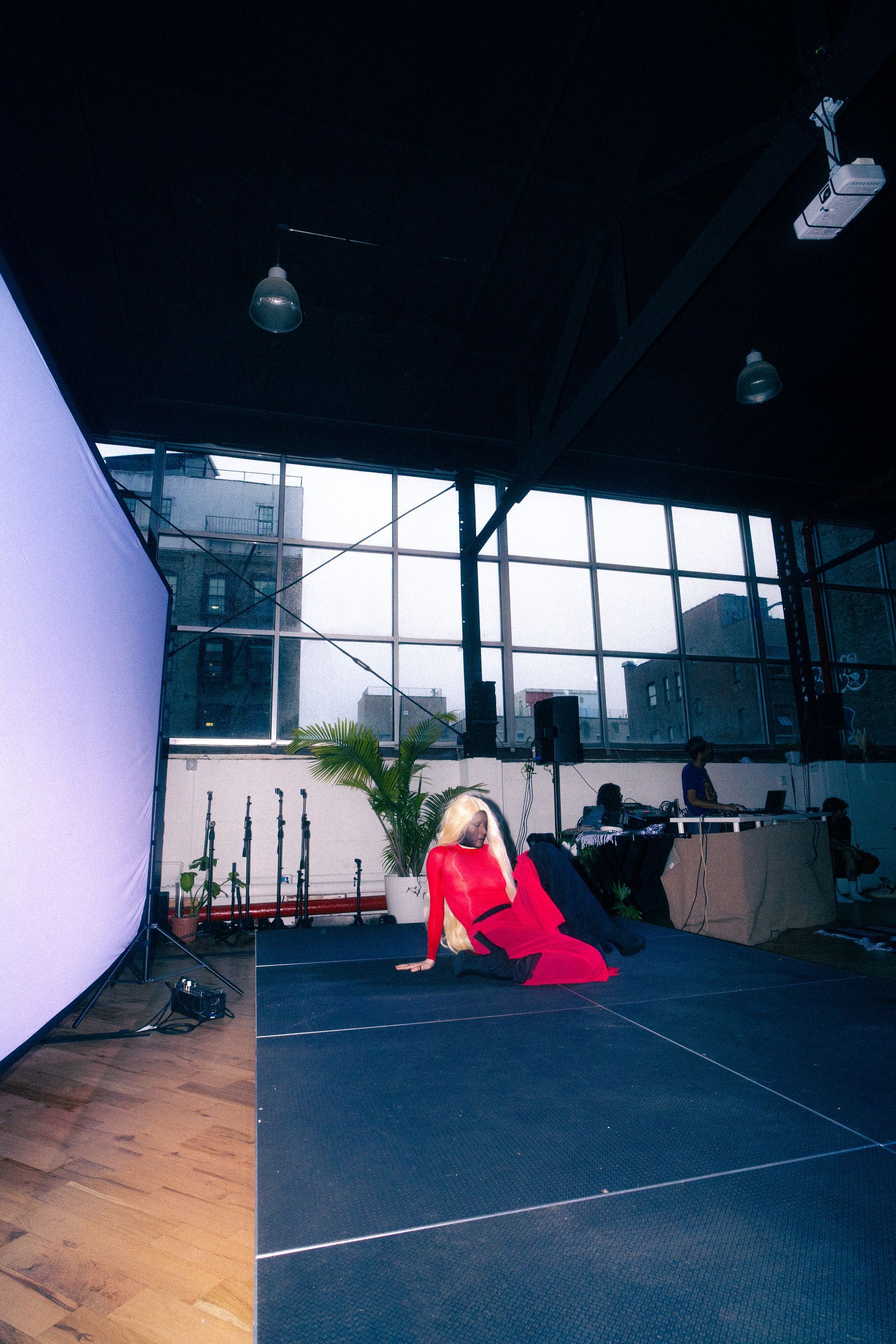A person in a red outfit kneels on stage. Large screen and cityscape background.