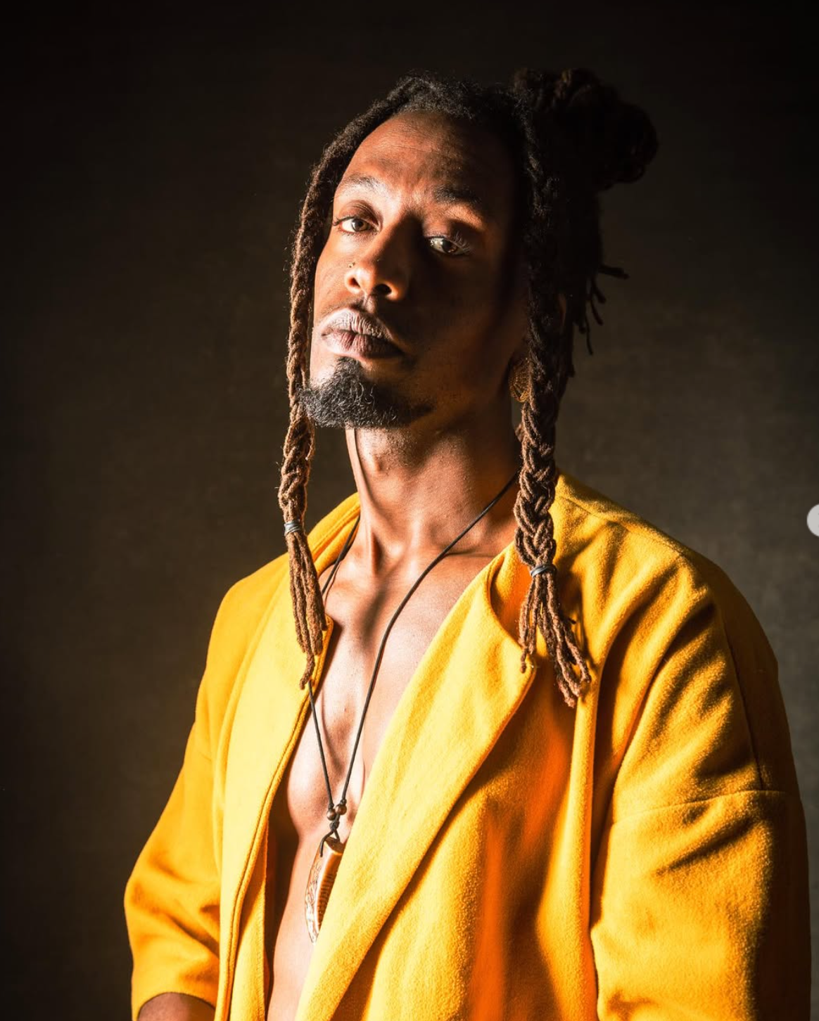 Man with dreadlocks and yellow jacket looks intently at the viewer.
