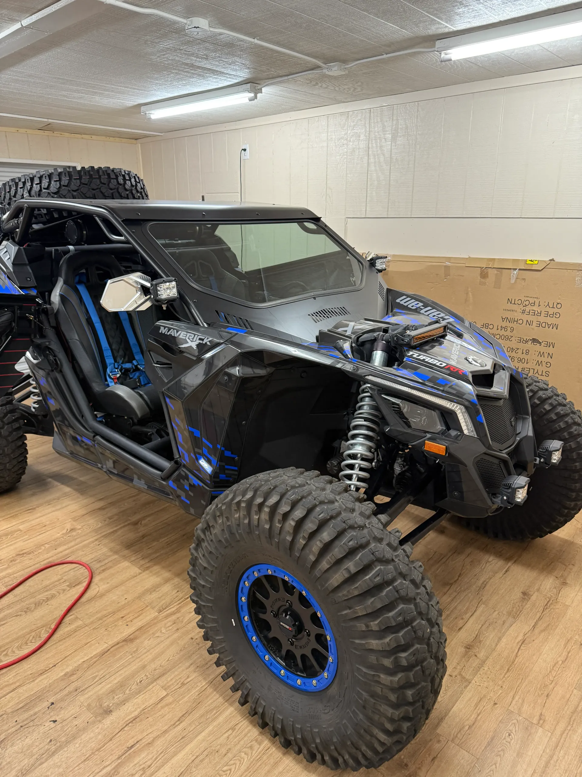 Black and blue off-road vehicle with large tires. Spare tire mounted on roll cage, indoors.