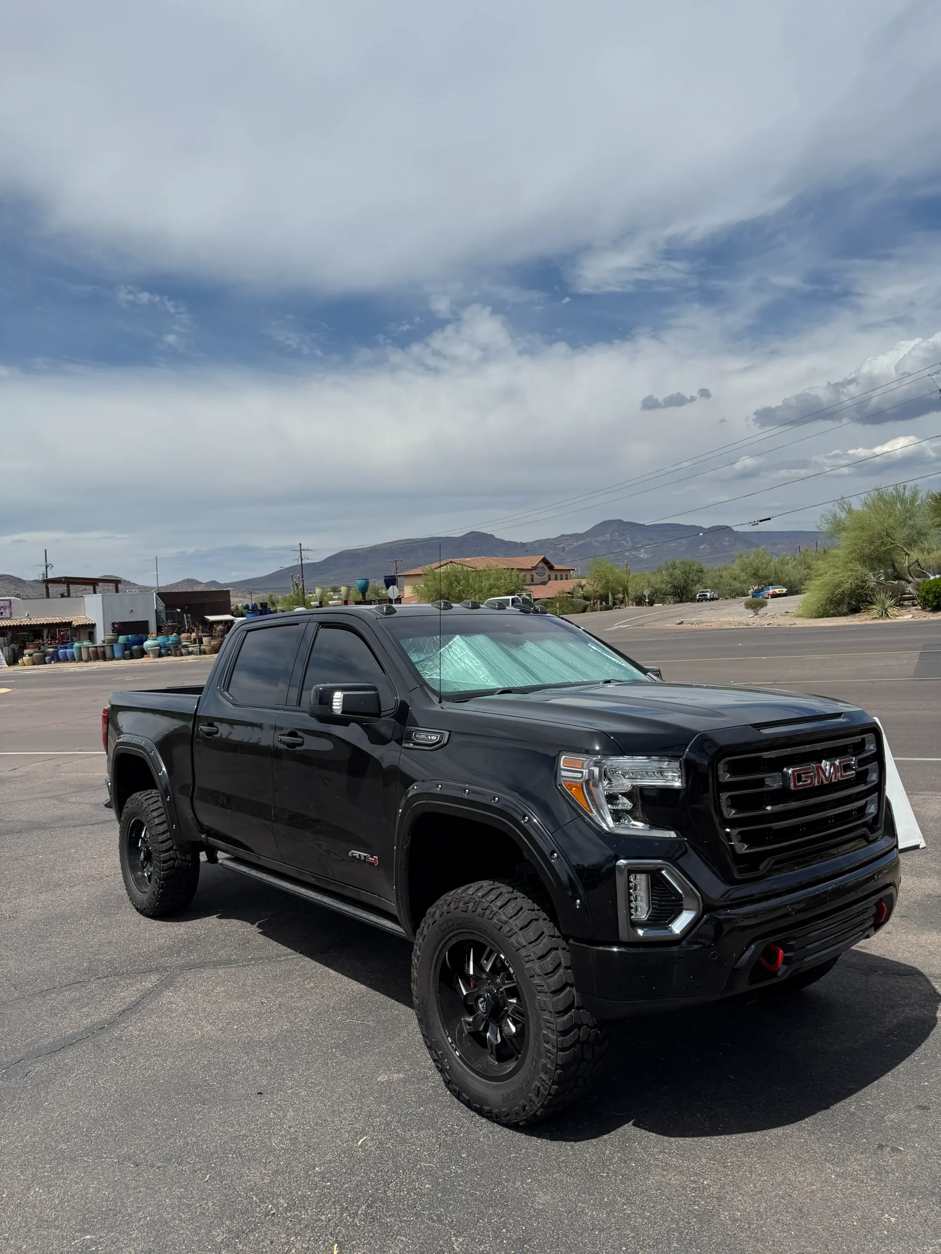 Black GMC Sierra truck parked under a cloudy sky, with mountains in the background.